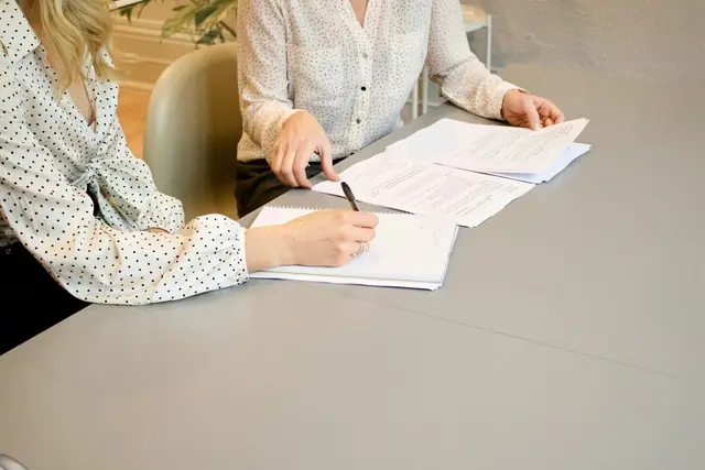 Dos personas revisan y firman papeles en una mesa.